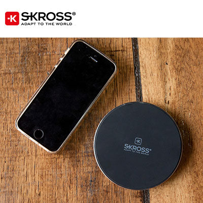 Round black SKROSS Wireless Charger 10 beside a smartphone on a wooden surface