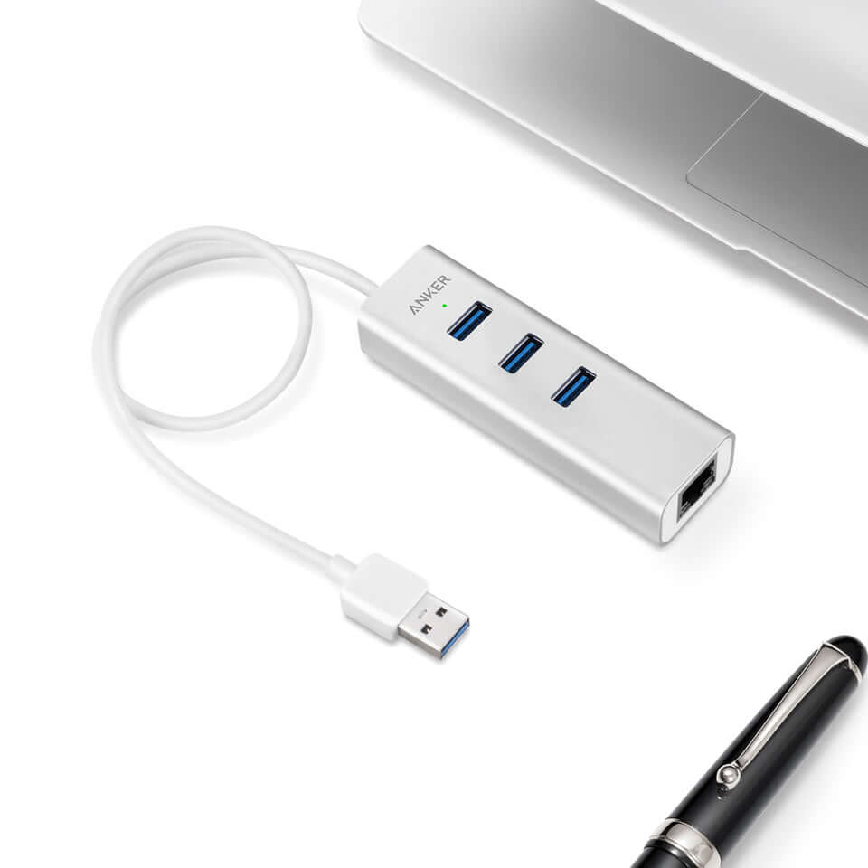 Silver Anker three-port USB and Ethernet hub with coiled attached USB-A lead beside a laptop.