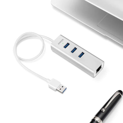 Silver Anker three-port USB and Ethernet hub with coiled attached USB-A lead beside a laptop.