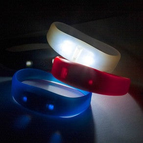 White, red and blue silicone wristbands shown with illuminated LED points against a dark background