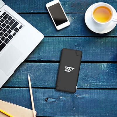 BrandCharger iQ+ powerbank with sample logo on a desk beside a laptop, phone and cup
