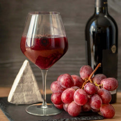 Luigi Bormioli Atelier 610ml Wine Glass filled with red wine next to grapes and a wine bottle.